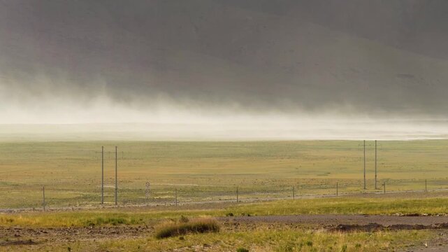 Sand storm moving by wind on grass field like wall with mountains background, 4k slow motion footage environment concept b roll shot.