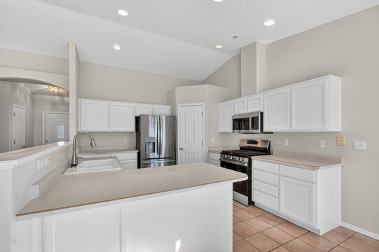 Bright modern kitchen interior with white paneled cabinets, stainless steel refrigerator plus stove