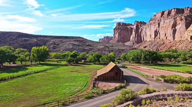Rustic pioneer barn stands in green pastures framed by towering red sandstone cliffs along Scenic Drive in Capitol Reef National Park Utah