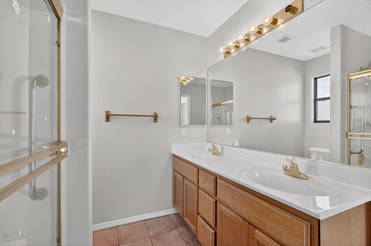 Bathroom with double sink vanity brass fixtures large mirror glass shower light neutral tones