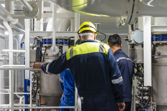 Marine engineers seen from behind while carrying out routine maintenance work in a ship's engine room, highlighting teamwork, technical operations and maritime engineering.