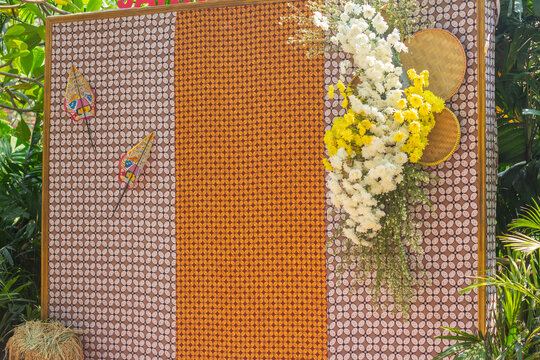 Traditional Javanese cultural photo backdrop decorated with batik fabric patterns, wayang puppets, and fresh yellow flower arrangement
