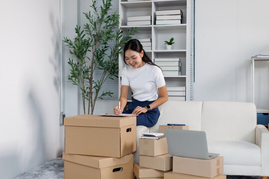 Young asian woman working from home, managing her e commerce small business, processing orders, packing shipping boxes for online retail delivery and logistics
