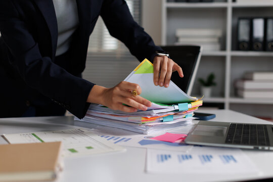 Businesswoman hands sorting through a big pile of official documents, files, and financial papers on an office desk, managing administrative tasks and data analysis