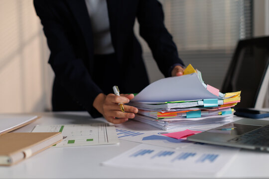 Businesswoman managing heavy workload, organizing documents, filing paperwork, handling reports, and processing data in a busy office environment during a demanding work day
