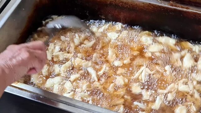 sliced cassava being deep fried in hot oil, showing a traditional cooking process with golden slices, bubbling oil, and crispy food texture. Advertisement culinary poduct