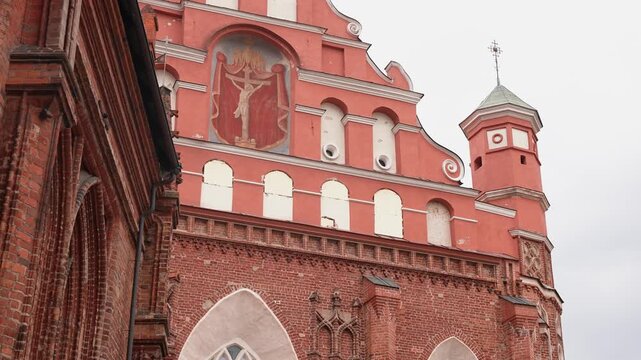 Impressive red brick church with ornate Gothic windows and tower, captured in daylight with soft clouds. Dynamic wide angle shot slowly pans upward, highlighting detailed architecture.