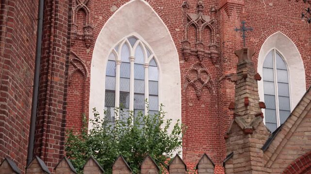 Crisp daylight close-up of the Church of St. Francis and St. Bernardino, Vilnius, with red brick Gothic architecture, pointed arched windows, masonry cross, lush greenery, and textured details.