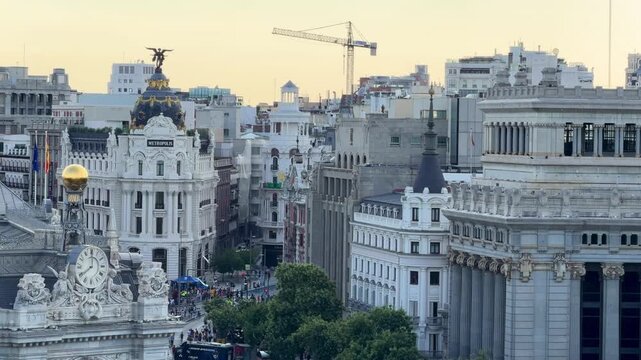 Madrid cityscape featuring the iconic Metropolis Building at Gran V&iacute;a and Calle de Alcal&aacute;, historic Beaux-Arts architecture framed by bustling streets and urban skyline at sunset
