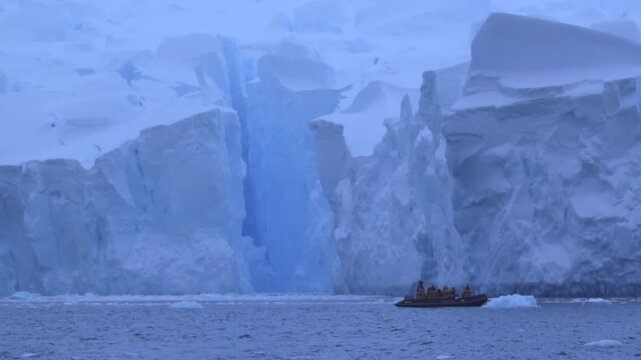 People in a Zodiac at the foot of a glacier towering over them on the Antarctic Peninsula