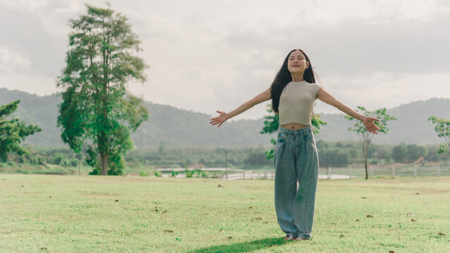 Young woman experiencing gratitude and happiness during outdoor portrait session in meadow with arms outstretched feeling peaceful breeze in warm sunlight shining down from sky
