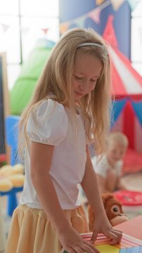 Girl places hands on a wooden rainbow puzzle on a red table in a playroom; concentration family bond.