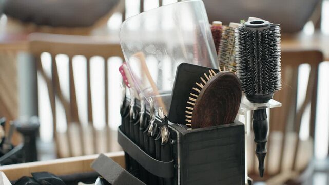 Camera moves across organized salon toolkit holding round brushes combs and clips in wooden holder at salon