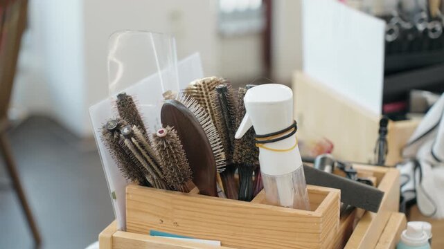 Wooden box holds collection of round hair brushes and spray bottle as camera pans across salon styling tools