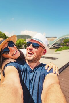 Happy young couple taking selfie in front of rike bridge in Georgia capital Tbilisi in summer. Two tourists having fun on romantic vacation, Holidays and traveling lifestyle concept.Weekend get away. Tbilisi. Georgia