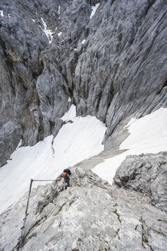 Mountaineer with helmet in a secured via ferrata, Zugspitze via ferrata, ascent to the Zugspitze, view of mountain basin with snow field of the H&ouml;llentalferner and H&ouml;llental, Wetterstein range, Bavaria, Germany