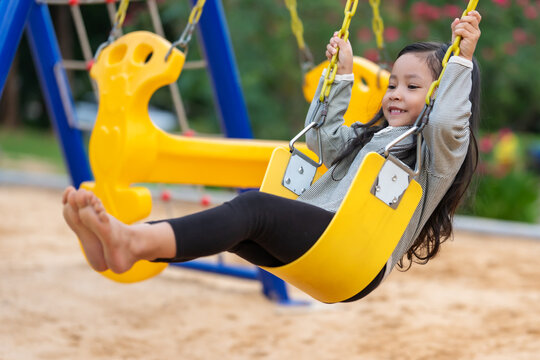 happy preschool child girl swinging on swing set at outdoor playground
