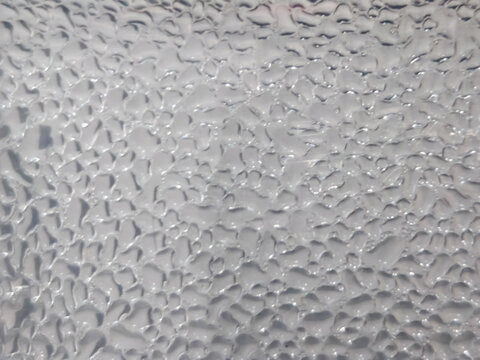 Macro background texture of natural water condensation and moisture droplets forming on a transparent glass surface, creating a pure, abstract, wet liquid pattern.