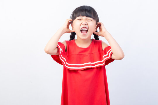 Angry little girl shouting out loud while covering her ears on a white background.