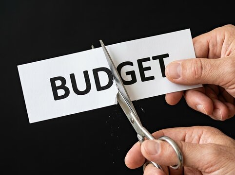 Hands cutting paper with word budget suitable for financial media representing cost reduction spending control and economic pressure