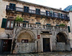 The ornate stone facade of the historic baroque Bizanti Palace features stone loggias, balustrades, and green window shutters in Kotor, Montenegro. © Gregory