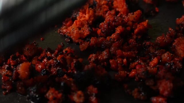 Close-up of a chorizo ​​sausage moving across a dark surface. A spatula moves through a mixture with a coarse texture and a spicy appearance. Footage ideal for recipes.