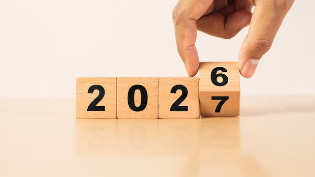 Hand turning wooden number block from 2026 to 2027, representing New Year transition, business planning, financial goals, future strategy, annual growth, change and new opportunities.