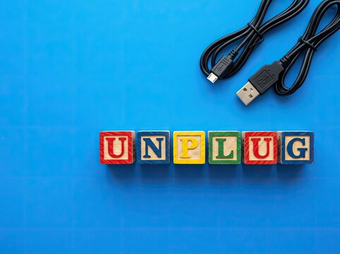 Wooden blocks spelling unplug next to disconnected USB cables ideal for wellness content representing digital detox mental rest and offline life