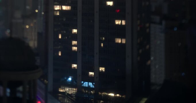 Timelapse shows lights switching on and off inside the windows of a modern skyscraper facade at night with tilt shift blur in Shanghai, China
