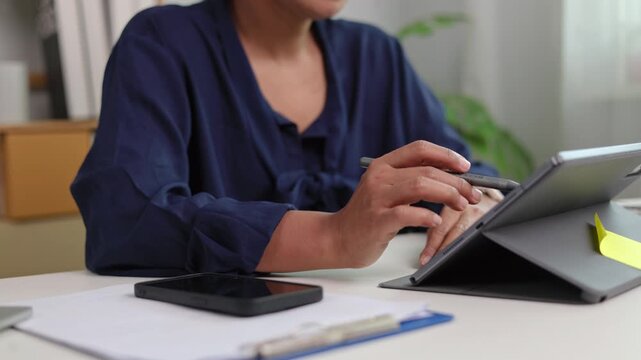 Smart female architect designing architectural draft on high tech tablet screen using stylus pen while sitting comfortably at bright office desk in daylight conditions indoor