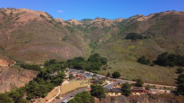 Elevated oblique aerial view showing rugged coastal hills and rolling ridgelines with patchy grass and chaparral above small developed area at base of cliffs. Big Sur, Rugged Point, California,