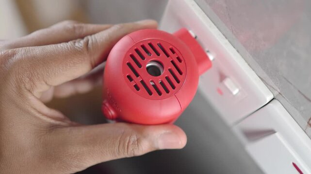 A person is plugging electric mosquito repellent plug-in machine into a wall socket in a home