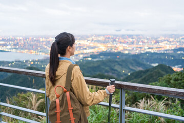 Obraz premium Profile view of female hiker holding trekking poles looking at Taipei view