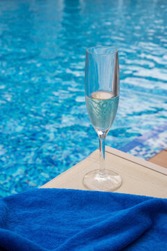 A glass of champagne and a blue towel by a swimming pool.