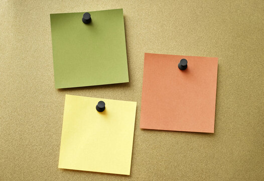 Colorful sticky notes pinned on a textured gold cork board for office organization.
