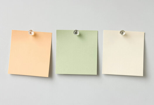 Three colorful sticky notes pinned on a grey wall for office organization and reminders.
