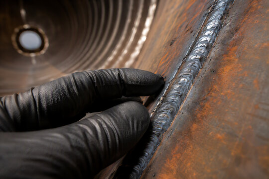 Black gloved hand touching corrugated rusty corroded metal surface inside industrial confined space