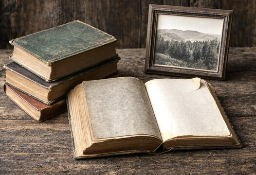 Vintage open book with old leatherbound volumes and framed mountain landscape photograph on rustic wooden table