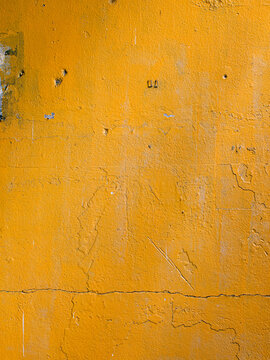 Weathered Orange Yellow Textured Concrete Wall with Cracks and Peeling Paint