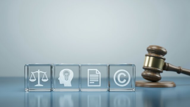 Wooden judge gavel next to glass cubes with intellectual property icons on a reflective table. Legal concept for copyright protection and patents.