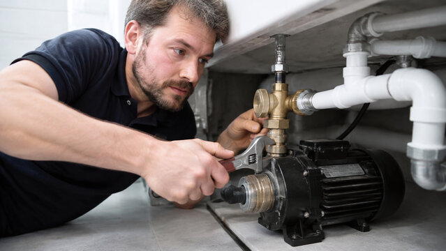 Professional plumber using a wrench to repair a domestic water booster pump