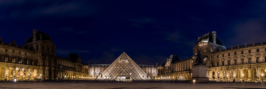Louvre Museum illuminated at night in Paris, France, with the iconic glass pyramid and historic palace architecture reflected in the courtyard