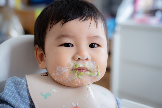Asian Baby Using Finger to Feed Herself a Food with Baby Led Weaning Concept.Cute Asian baby boy eating finger food in high chair.	
