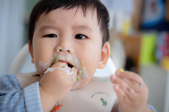 Asian Baby Using Finger to Feed Herself a Food with Baby Led Weaning Concept.Cute Asian baby boy eating finger food in high chair.	