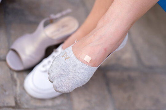Woman sticking medical patch on foot callus. Concept: First aid plaster treatment, Pharmacy care skin health, Uncomfortable shoes problem retail. 