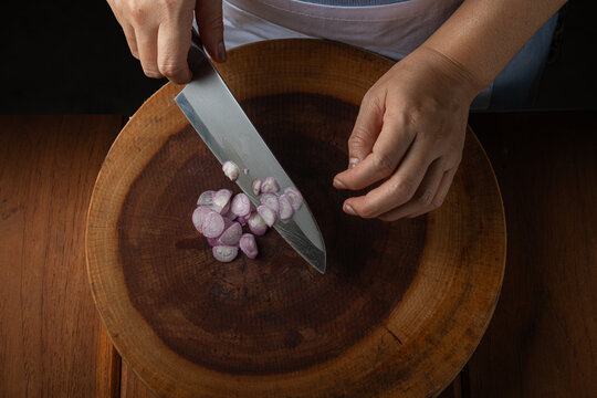 Top view close up of chef using knife blade to gather sliced shallots on board.