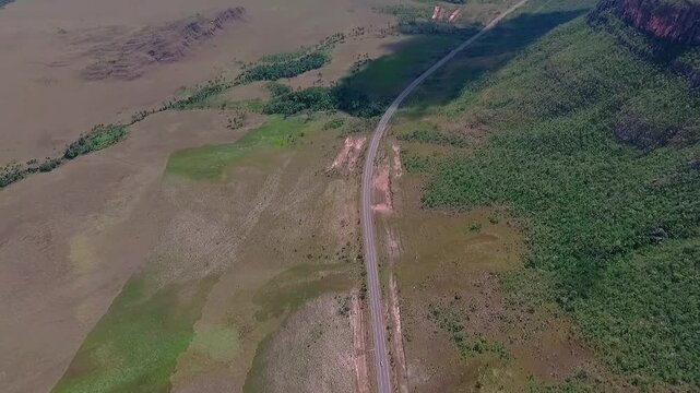 GO-239 crosses the Cerrado beside Morro da Baleia in Alto Paraiso de Goias, Goias, Brazil, South America, revealing the Chapada dos Veadeiros plateau, high-altitude drone parallax pullback with tilt u