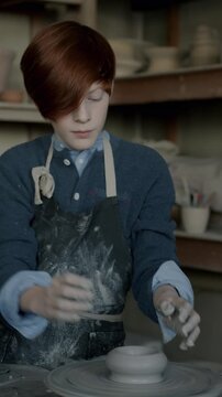 Serious child in apron making pot in workshop enjoying activity in leisure time. Pottery class and professional education concept.