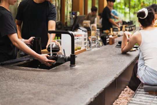 Barista rinsing ceramic tea bowls under running tap water in cafe.