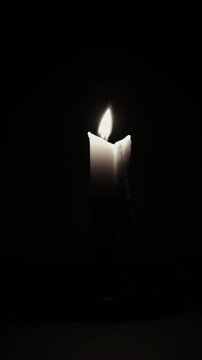 Close up shot of wax candle burning timelapse with flame glowing on wick in the dark creating mysterious scene background. Dim candle flame on black background time lapse.
